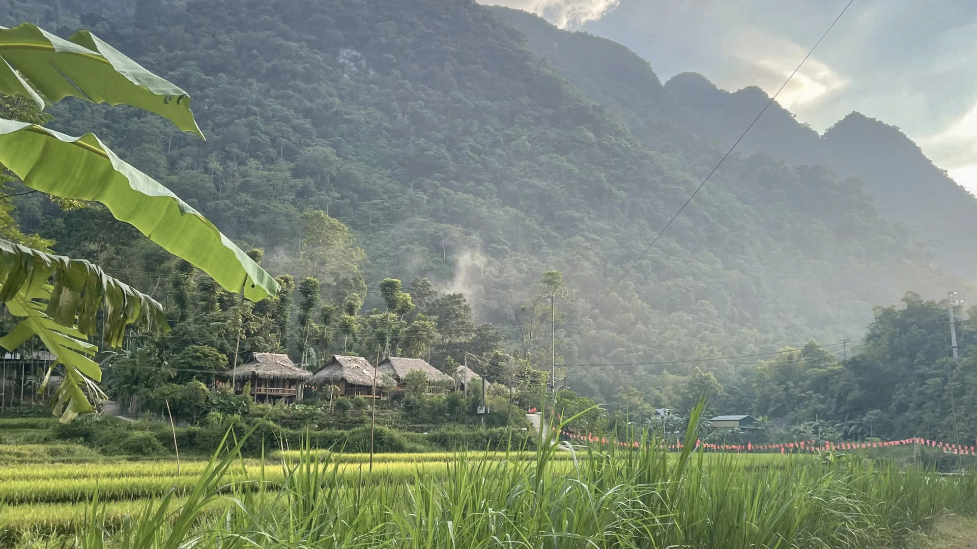Smoke rising between rice fields and forested mountains in Pu Luong