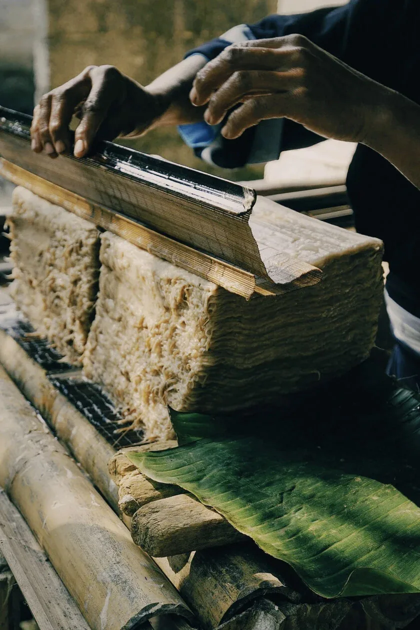 Hands and a wooden tool above a stack of handmade paper.